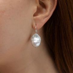 Brinco Luar com pérola natural pendurada no ouvido de mulher com cabelo castanho