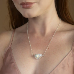 Colar delicado com pingente de pérola barroca em corrente prateada, usado no pescoço de mulher com vestido rosa claro