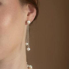Brinco Fleur Divine branco com pérolas e correntes finas penduradas na orelha feminina