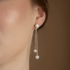 Brinco Fleur Divine branco com pérolas penduradas e correntes delicadas, usado em orelha feminina