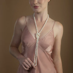 Mulher usando colar de pérolas branco estilo duas voltas com nó central, vestido rosa claro