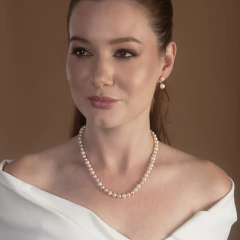 Mulher usando colar de pérolas em tons coral e brinco de pérola dupla