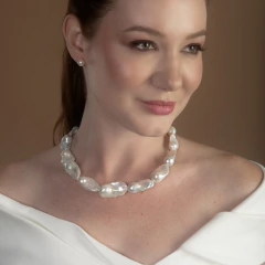 Mulher usando colar de pérolas grandes e irregulares, combinando com brincos de pérola, vestindo blusa branca