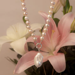 Colar de pérolas com pingente de pérola barroca, ao fundo flores rosa e branca desfocadas