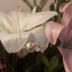 Colar Pétalas Rose com pérola iridescente em corrente delicada, ao fundo flores brancas e rosas desfocadas