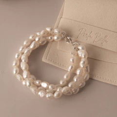 Pulseira Verano composta por três fileiras de pérolas brancas naturais usadas no pulso de uma pessoa com camiseta roxa