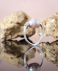 Anel Santorini com pérola rosa e estrutura de prata, refletindo sobre uma superfície espelhada.