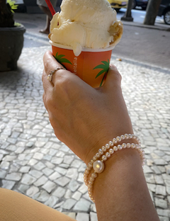 Pulseira Bela com pérolas em um braço segurando um copo de sorvete.