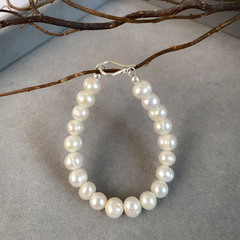 Pulseira Lua M em pérola, adornando o pulso de uma modelo, com blusa azul listrada ao fundo.