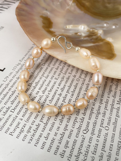 Pulseira de pérolas em tons suaves, destacando-se sobre uma página de livro.