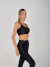 Mulher usando legging preta de cintura alta e top esportivo preto, posando de perfil