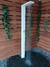 Ducha de piso em aço inox branca para área externa, instalada em um ambiente com paredes de madeira e plantas ao redor.