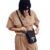 Mulher usando um conjunto de roupa bege e um gorro preto, colocando um celular em uma bolsa preta da marca Stüssy.