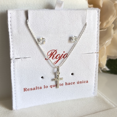 Set de joyería que incluye aretes y un collar con un colgante en forma de cruz, en un fondo blanco con detalles en rojo.