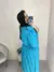 Vestido Mirella Plus Size em tom azul, com detalhes em poá, sendo usado por uma mulher que se vê de perfil em um espelho.