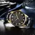 Relógio Curren masculino elegante com mostrador preto e detalhes em dourado, sobre superfície de couro.