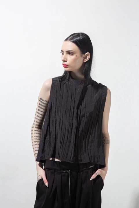 Modelo con blusa negra sin mangas de tela texturada llamada Blusa Tsubaki, posando de frente con la cabeza girada hacia un costado.