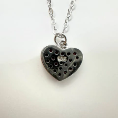 Detalle lateral del dije de corazón con zirconias rojas de N&Njoyeria mostrando el acabado pulido y la calidad del engaste.