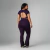 Mulher vestindo conjunto legging flare e top Gisele suplex poliamida plus cor grape, vista de costas, destacando o recorte nas costas do top.