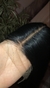 Close-up da lace frontal com repartição central e fios pretos lisos, destacando o acabamento natural da fibra premium sobre a mão da modelo. Detalhe da lace frontal com repartição central. Lace preta com acabamento realista na parte superior. Fibra premiu