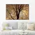 Quadro decorativo com galhos secos em um fundo laranja, pendurado em uma parede acima de um sofá claro.