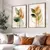 Dois quadros decorativos com ilustrações de folhas em tons de verde e laranja, emoldurados em madeira, decorando uma parede ao lado de um sofá com almofadas.