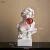 Escultura decorativa de uma figura feminina com uma bola de chiclete vermelha na boca, medindo 29cm de altura, 17,5cm de largura e 13cm de profundidade.