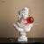 Escultura decorativa de um busto grego com uma bola de chiclete vermelha na boca, medindo 29 cm de altura, 17 cm de largura e 14 cm de profundidade.