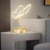 Luminária de mesa em formato de borboleta com base dourada, iluminada e posicionada ao lado de um sofá em um ambiente de quarto moderno.