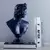 Escultura em busto de David em tons escuros, ao lado de livros empilhados em uma mesa.