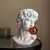 Escultura decorativa de um busto com aparência de mármore, inspirado em Michelangelo, com um chiclete vermelho na boca.