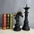 Escultura de xadrez em preto, apresentando uma peça de cavalo e uma peça de rainha, com detalhes em dourado. Ao fundo, livros decorativos.