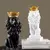 Escultura de leões imperiais, um em preto e outro em branco, ambos com coroas douradas, posicionados sobre livros de decoração.