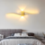 Arandela de parede ondular LED iluminando um quarto com cama e cabeceira cinza.