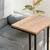 Mesa de arrime de diseño moderno, con superficie de madera clara y patas negras, ubicada junto a un sofá gris.