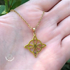 Colar Nó de Bruxa Dourado em aço inoxidável, pendurado na mão de uma pessoa, com detalhes em formato de estrela.