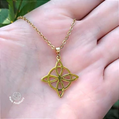 Colar Nó de Bruxa Dourado em aço inoxidável, pendurado na mão de uma pessoa, com detalhes em formato de estrela.