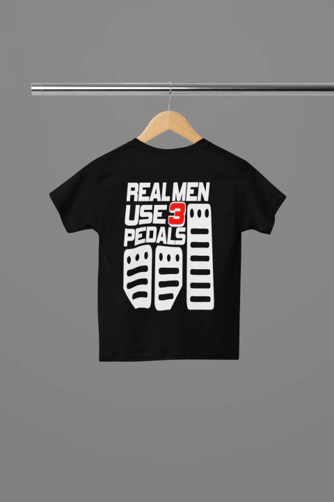 Camiseta infantil preta com a frase "REAL MEN USE 3 PEDALS" e desenhos de três pedais na parte de trás.
