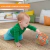 bebê segurando o Brinquedo infantil Oball Rollin Rainstick da Bright Starts, mostrando a bola colorida cheia de furos para agarrar e o tubo central de pau de chuva.