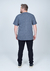 Camiseta Plus Size Malha Botonê na cor azul marinho vista de trás, usada por um homem com calças pretas.