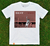 Camisa branca com estampa que destaca a palavra "BEST" e um jogador de futebol em ação, com o fundo de um campo e torcedores.