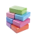 Seis ladrillos de yoga de goma eva en diferentes colores (verde, rosa, azul, lila y naranja) apilados sobre un fondo blanco.