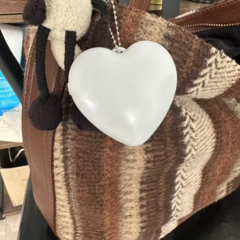 Luz para carteras, bolsos o mochilas en forma de corazón, color blanco, con cadena de sujeción plateada colgando de un bolso de cuero marrón.