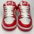 Imagem frontal do Tênis Nike Dunk Low nas cores vermelho e branco, com detalhes em couro e cadarços brancos.