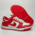 Tênis feminino Nike Dunk Low, modelo em vermelho e branco, feito de material sintético, posicionado com a parte frontal e a sola visíveis.