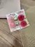 Conjunto de presilhas de cabelo douradas com pompons rosa e vermelho, em embalagem de papel.