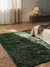 Alfombra rectangular Lisa de color verde, colocada en un ambiente acogedor con luz natural y decoraciones minimalistas.