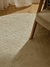 Alfombra circular Lisa de color beige con textura suave, ubicada en un ambiente luminoso junto a una silla de madera.