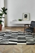 Alfombra Urban Stripe en blanco y negro con diseño de rayas, ubicada en un ambiente moderno con una silla negra y decoración minimalista.