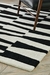 Alfombra Urban Stripe con diseño de rayas en blanco y negro, colocada en un suelo de madera.